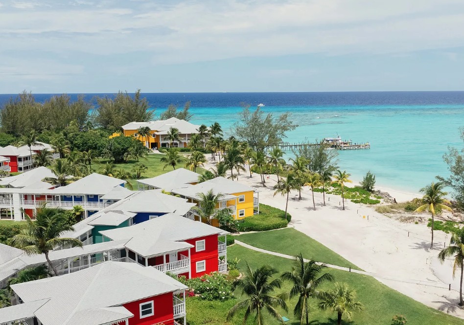 Bangalôs coloridos do Club Med Columbus Isle na praia branca das Bahamas, com píer e mar turquesa