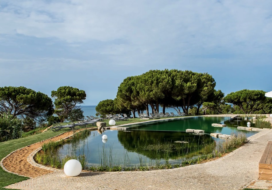 Piscina biológica do Club Med Da Balaia cercada de pinheiros-mansos e vista para o mar do Algarve