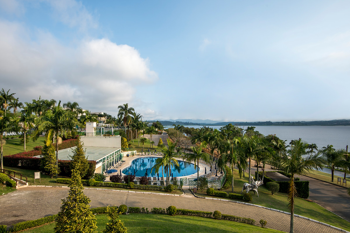 Piscina e gramado do Club Med Lake Paradise à beira do lago, com palmeiras e serra ao fundo