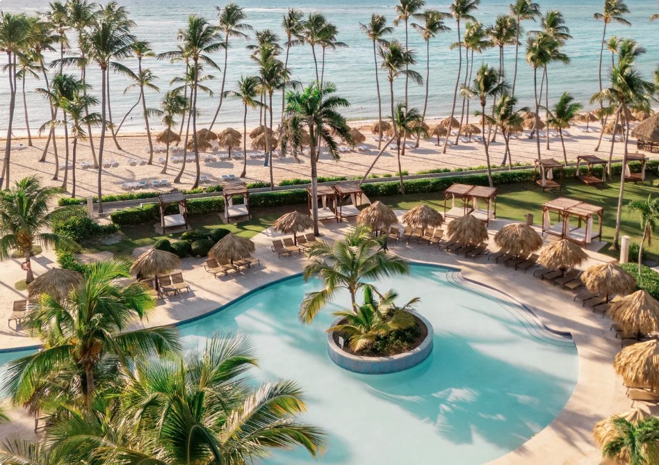 Vista aérea da piscina com ilha de palmeiras no Club Med Punta Cana, praia branca e mar turquesa