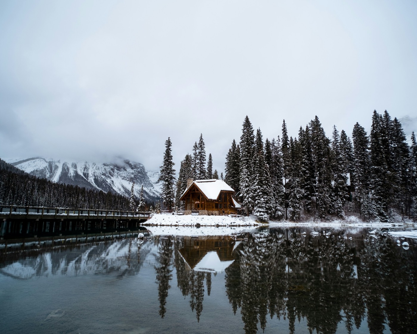 Cabana de madeira à beira de um lago congelado, cercada por floresta boreal nevada no Canadá