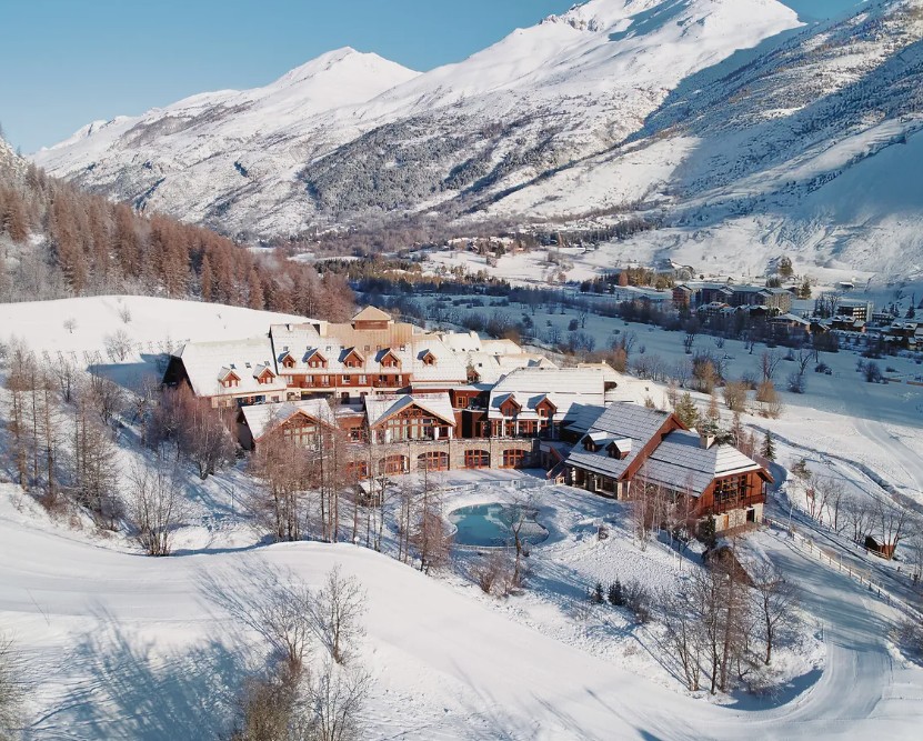 Village alpino de Serre Chevalier na neve, com piscina circular turquesa no pátio e picos ao fundo
