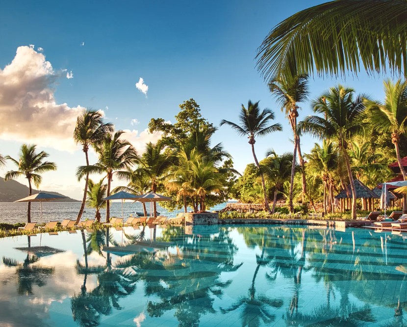 Piscina infinita do Club Med Seychelles ao entardecer, palmeiras refletidas e ilha ao fundo