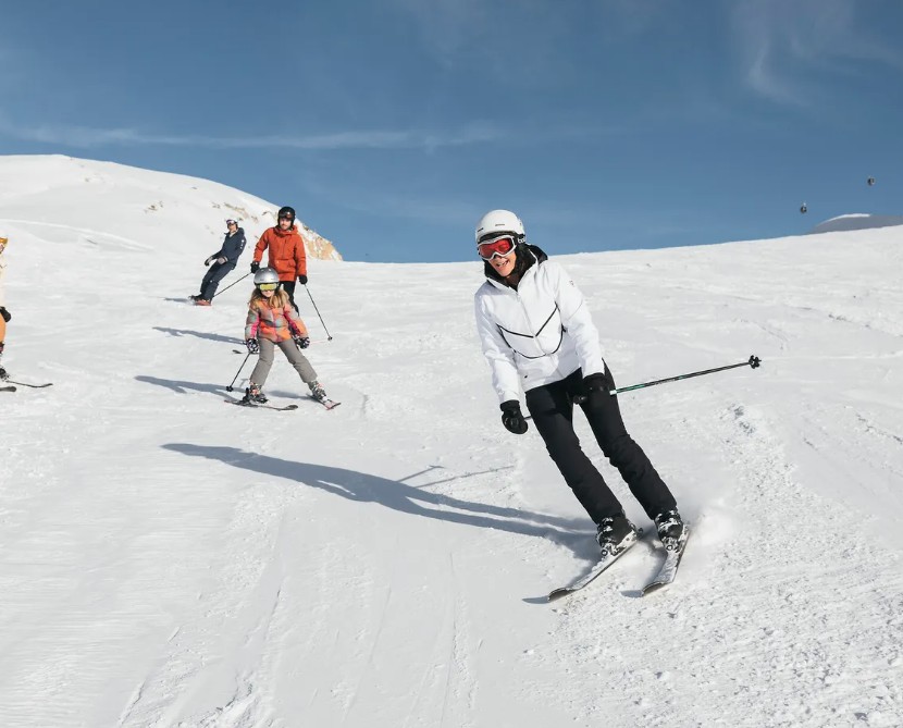 Esquiadores numa pista ensolarada de Tignes, com céu azul e teleférico ao fundo
