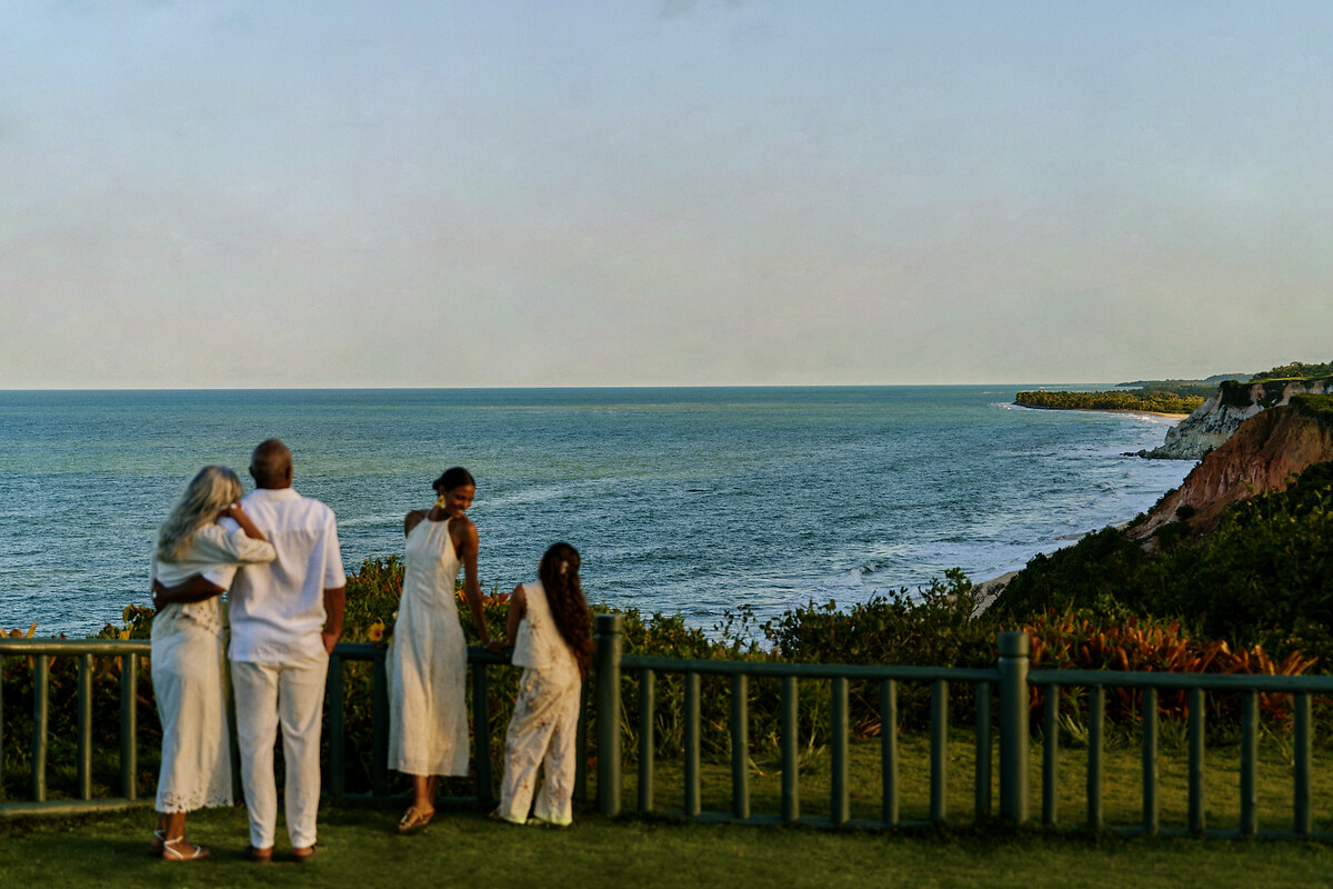 Família na gramada da falésia de Trancoso olhando o mar turquesa e as falésias da costa baiana